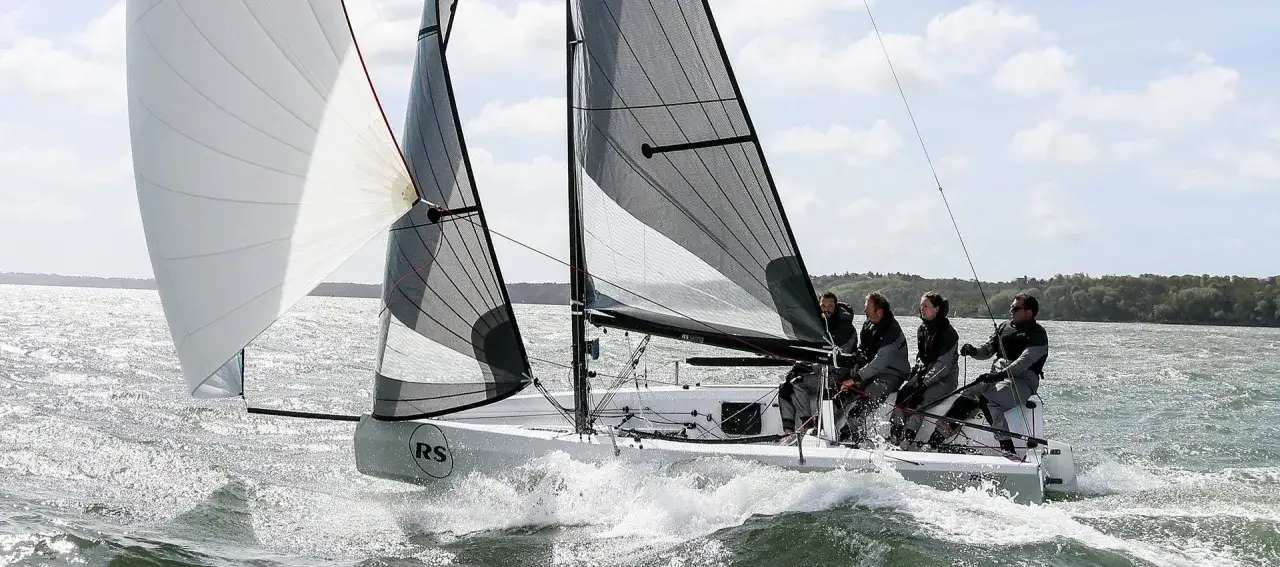 Equipaggio sull'RS 21, con vele spiegate, solca le onde con un'aria di concentrazione e determinazione.