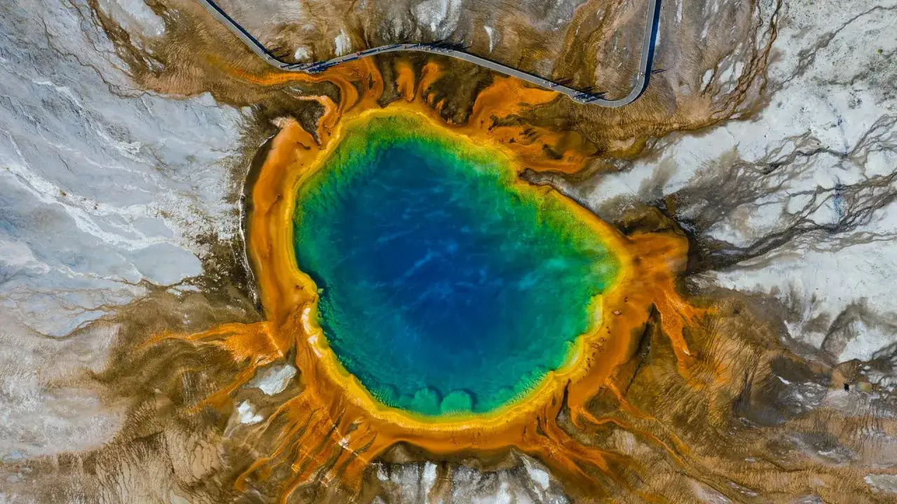 Der Grand Prismatic Spring im Yellowstone Nationalpark, ein farbenprächtiges Naturwunder mit tiefblauem Wasser, umgeben von leuchtenden Ringen aus Grün, Gelb und Orange.