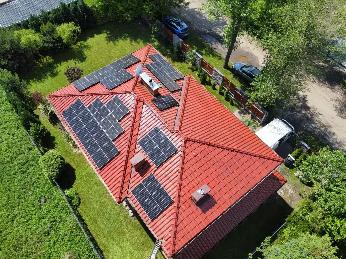 Dach z panelami fotowoltaicznymi, kiedy przepada energia z fotowoltaiki, dom z zielonym ogrodem i samochodami na podjeździe.