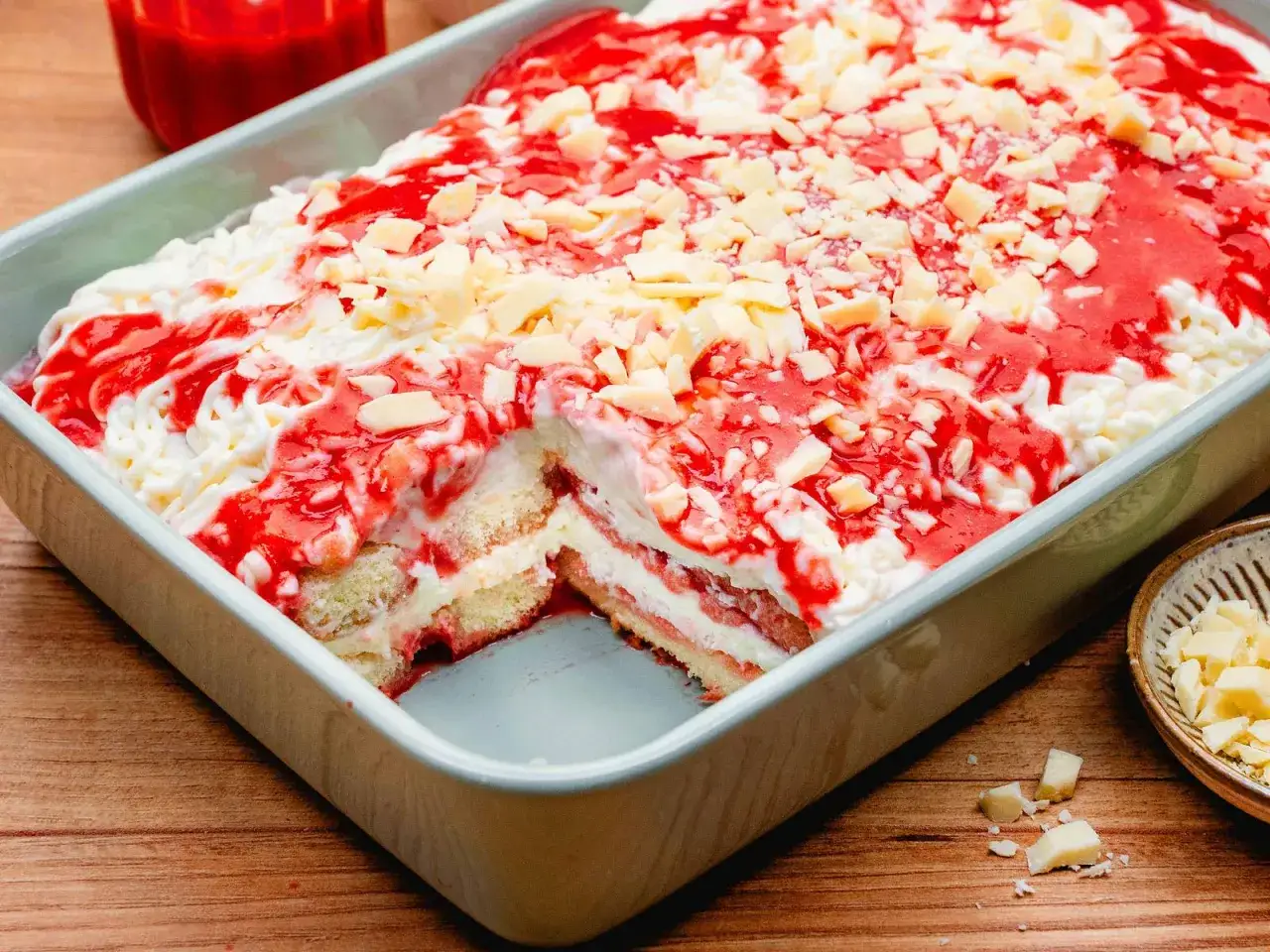 Ein k&ouml;stliches Dessert, das an Spaghetti-Eis und Tiramisu erinnert, mit Schichten aus Biskuit, Creme und Erdbeersauce, bestreut mit wei&szlig;en Schokost&uuml;ckchen.