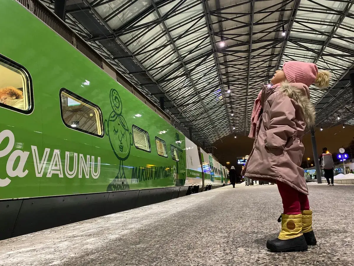 Ein M&auml;dchen in Winterkleidung blickt erwartungsvoll zum gr&uuml;nen Zug in Finnland.