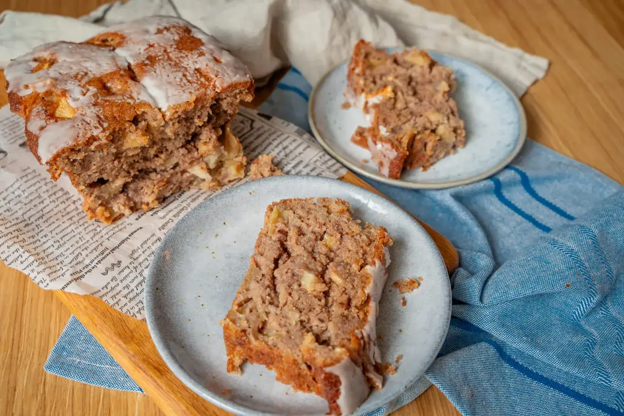 Saftiger Apfel Walnuss Kuchen mit Zuckerguss, auf Zeitungspapier und blauer Serviette angerichtet. Ein St&uuml;ck auf einem Teller.