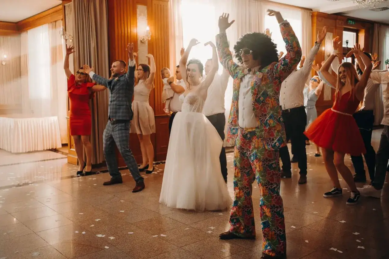 Szalona zabawa weselna! Goście tańczą w rytm muzyki na wesele, a jeden z nich w kolorowym garniturze disco przyciąga wzrok.