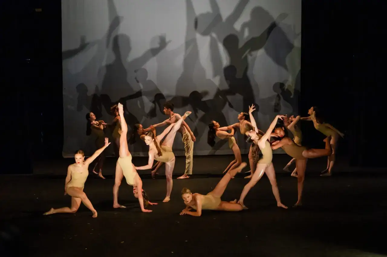 Giovani ballerini in scena, in pose dinamiche e aggraziate, durante i **corsi di danza moderna**. Le ombre sullo sfondo amplificano l'effetto scenico.