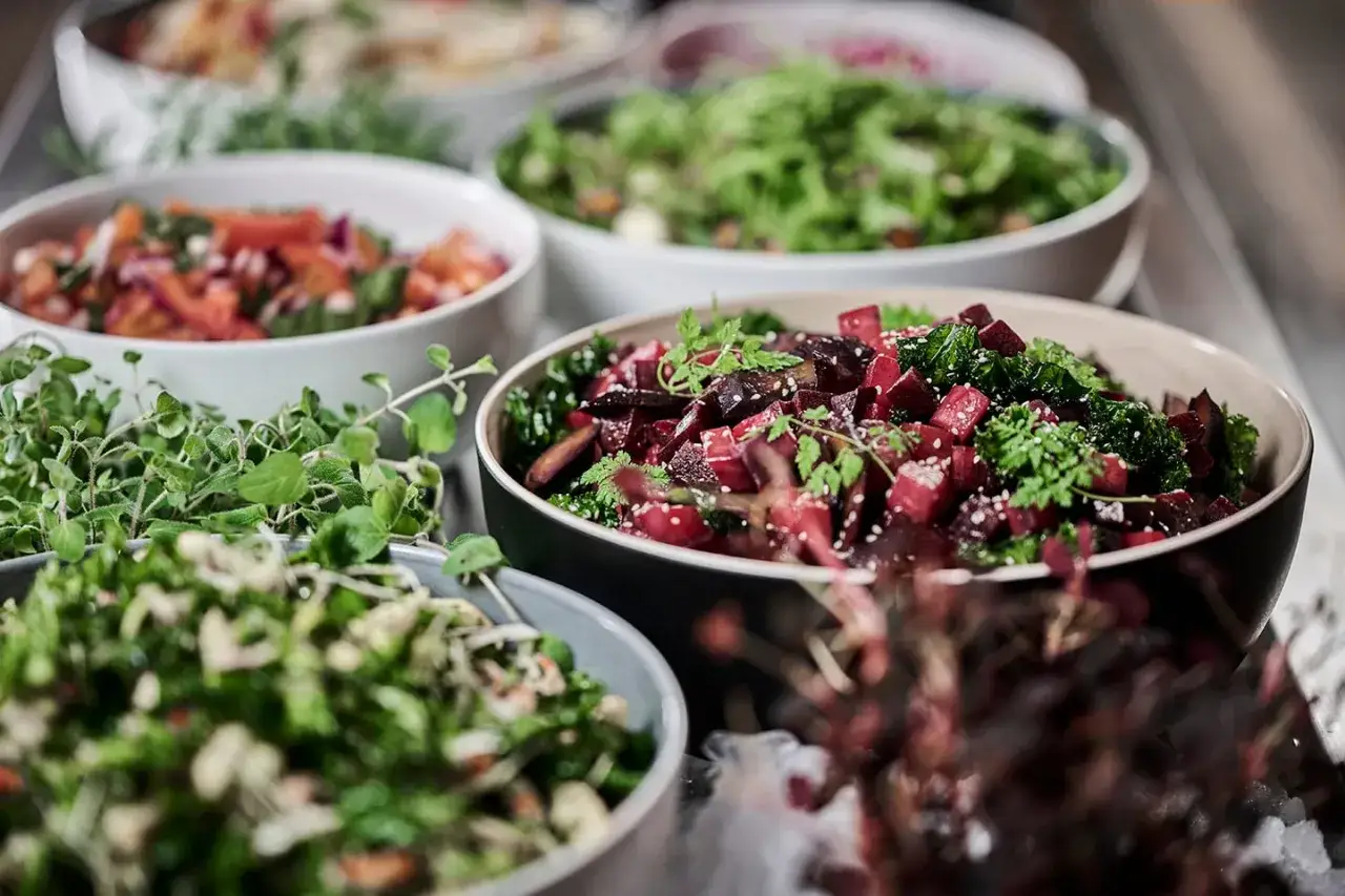 Flera skålar med färgglada sallader, perfekt som sallad till paj. En skål med rödbetor och grönkål, en med tomat och lök, och en med gröna blad.