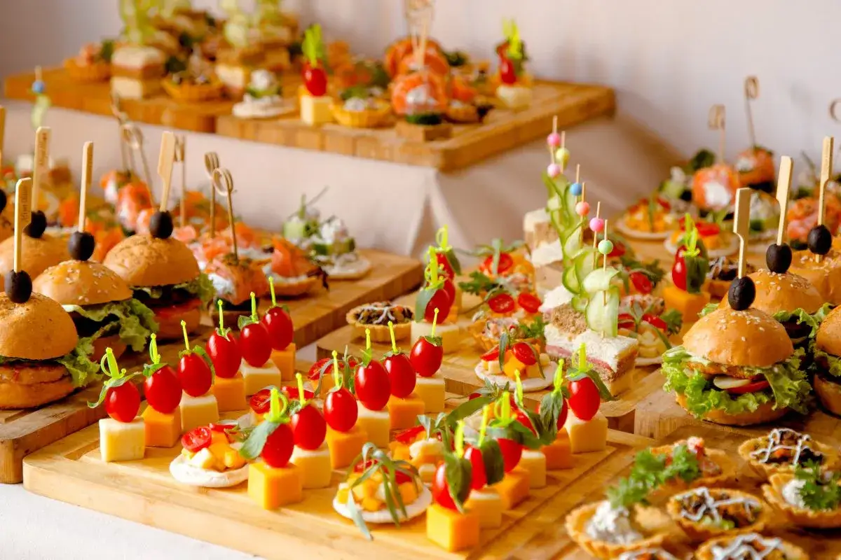 Bandejas con elegantes aperitivos para bodas: mini hamburguesas, sándwiches, canapés de salmón y brochetas de tomate y queso.