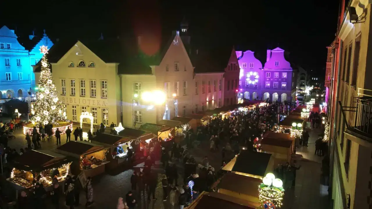Tłoczny jarmark bożonarodzeniowy w Olsztynie. Rozświetlona choinka, stragany i tłumy ludzi tworzą magiczną atmosferę.
