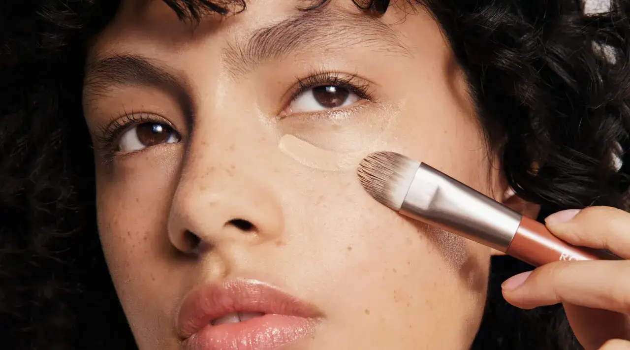 Nahaufnahme einer Frau, die mit einem Pinsel Concealer auf ihre Wangen auftr&auml;gt. Perfekte Concealer Anwendung f&uuml;r einen makellosen Teint.