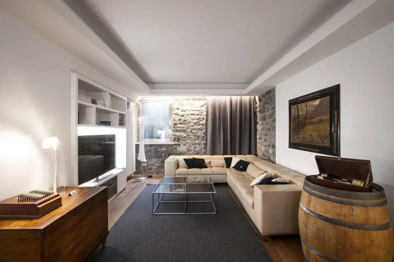 Soggiorno moderno con divano angolare beige, tavolini in vetro, mobile TV, libreria e botte di legno. Ecco come arredare un soggiorno con stile.