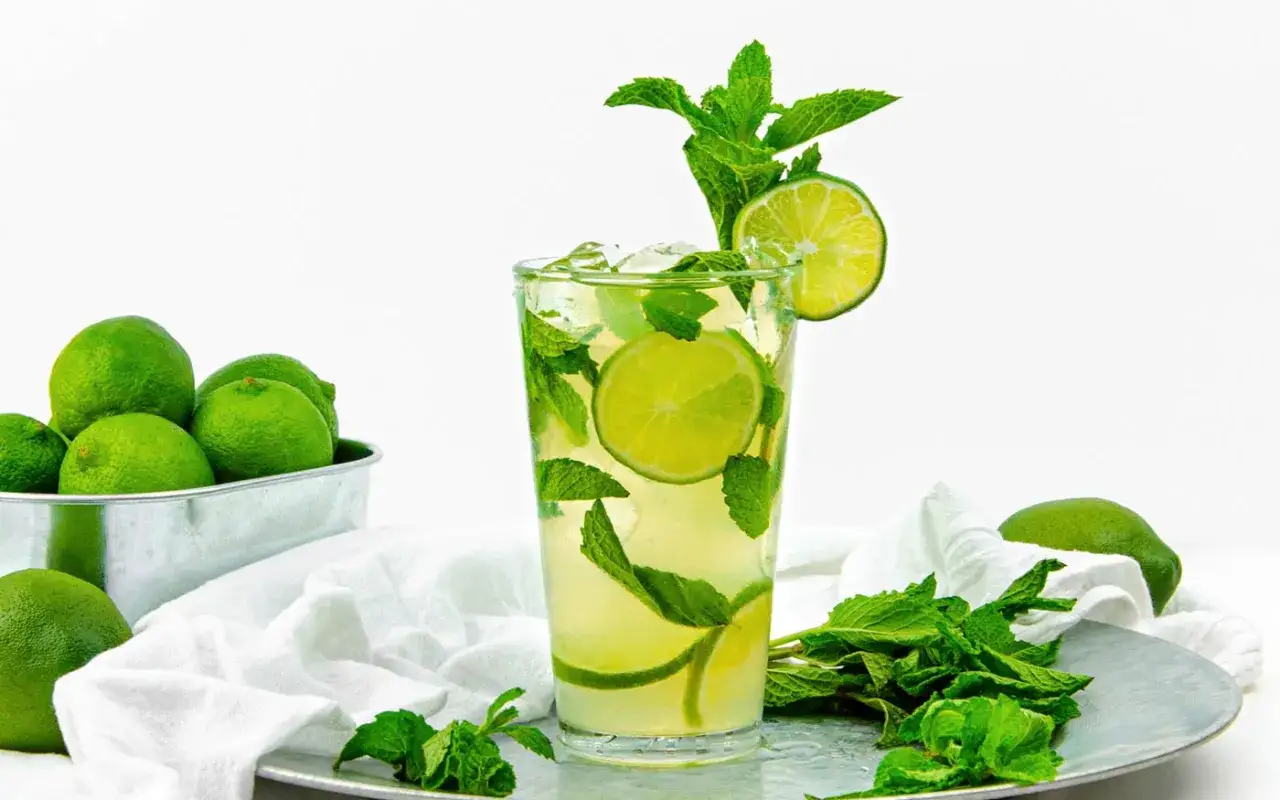 Orzeźwiający mohito z limonką i miętą, idealny na upalne dni. Obok limonki w metalowej misce i świeża mięta.