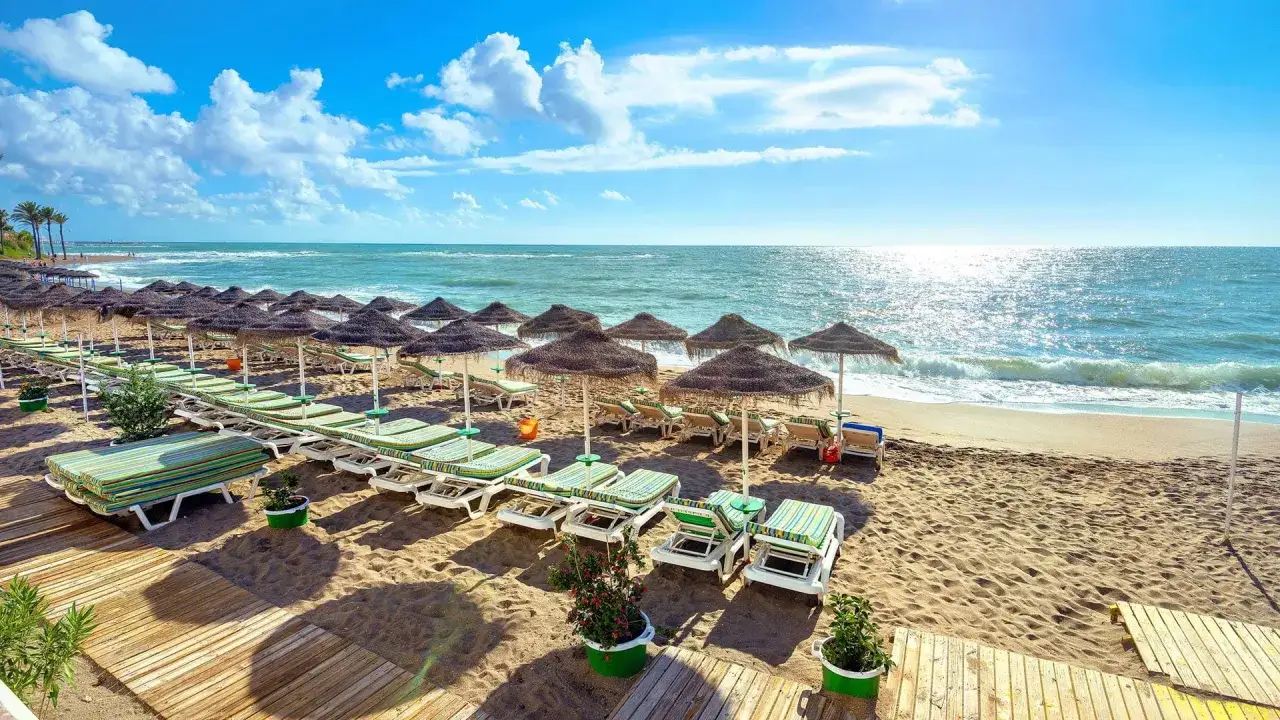 Słoneczna plaża w Maladze, idealna na lot z Berlina. Leżaki i parasole czekają na gości.