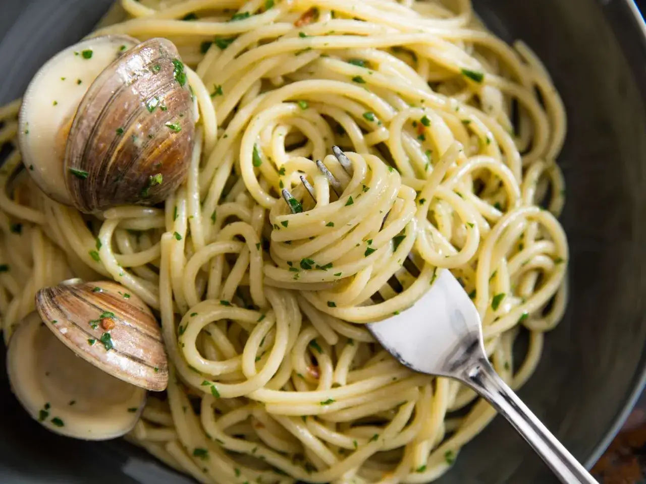En gaffel snurrar upp en perfekt portion pasta vongole, med musslor och persilja.