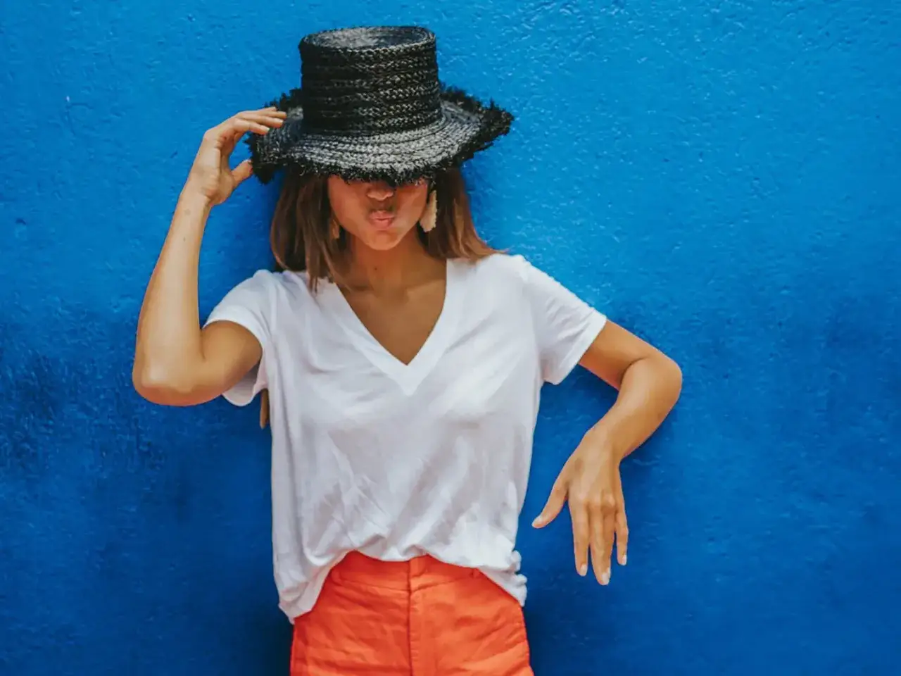 Mujer con sombrero negro y camisa blanca, un truco de estilo es llevar la camisa por dentro de los pantalones naranjas.