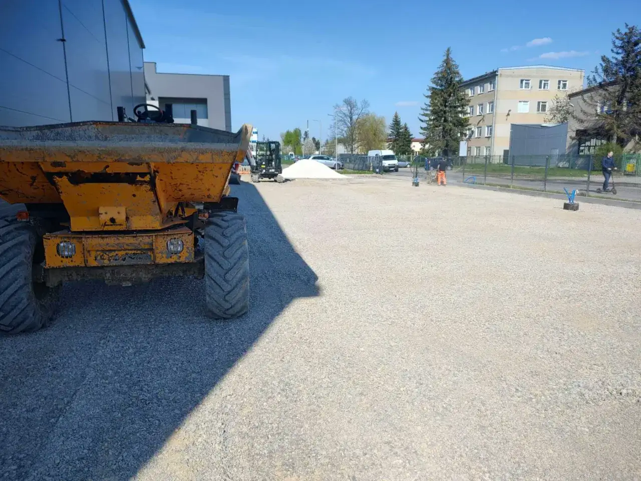Korytowanie pod parking, cena za m2. Żółta koparka i plac budowy z kruszywem.
