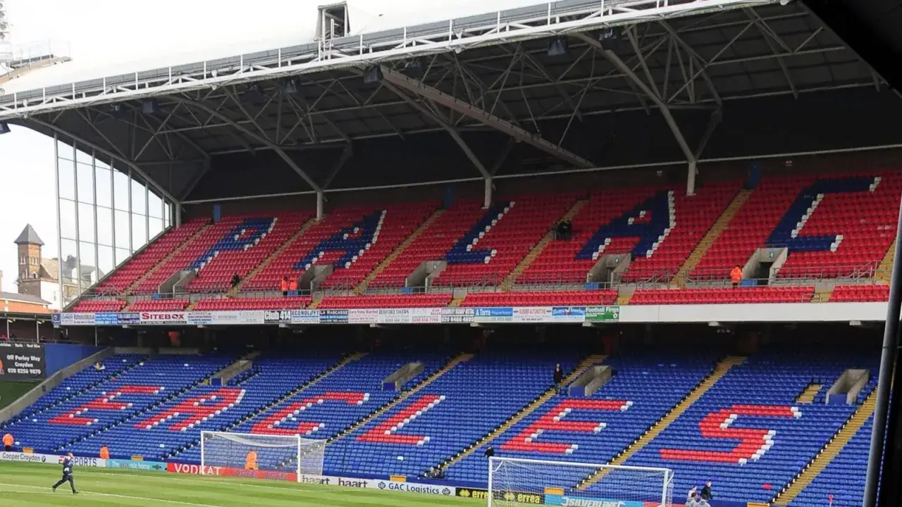 Trybuna stadionu Crystal Palace z czerwonymi i niebieskimi siedzeniami tworzącymi napisy. Fani czekają na nowe crystal palace transfery.