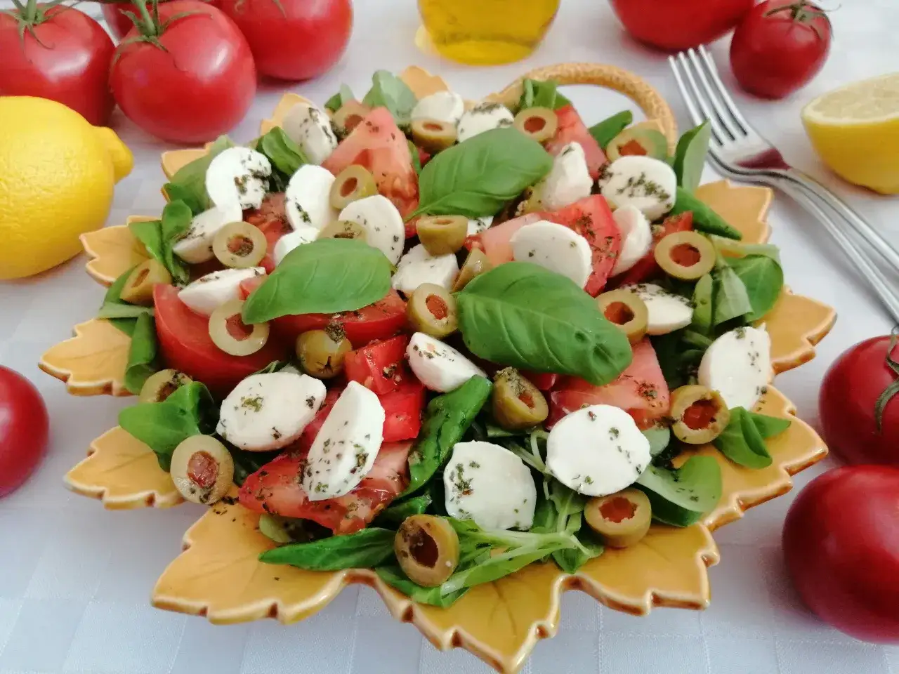 Sałatka caprese z pomidorami, mozzarellą i oliwkami, ozdobiona bazylią. Idealna do dodawania do dań letnich.