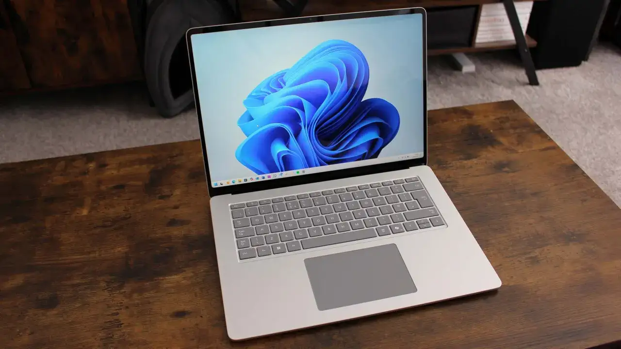 Srebrny laptop z systemem Windows 11 ARM na drewnianym stole.