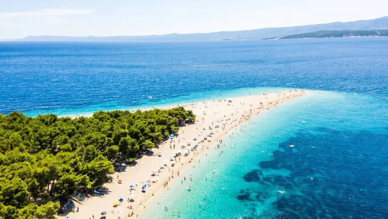 Plaża w kształcie rogu obfitości na chorwackim morzu, pełna ludzi i zielonych drzew.