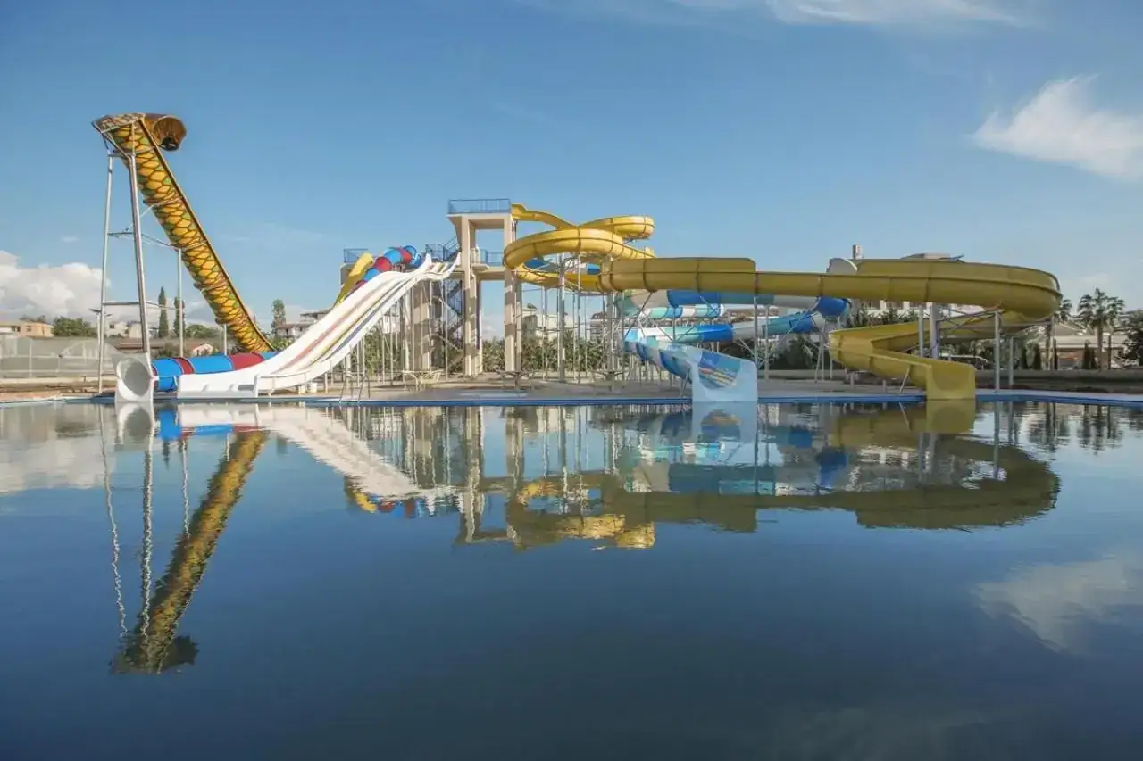 Kolorowe zjeżdżalnie wodne w Xafira Deluxe Resort & Spa odbijają się w spokojnej tafli basenu.