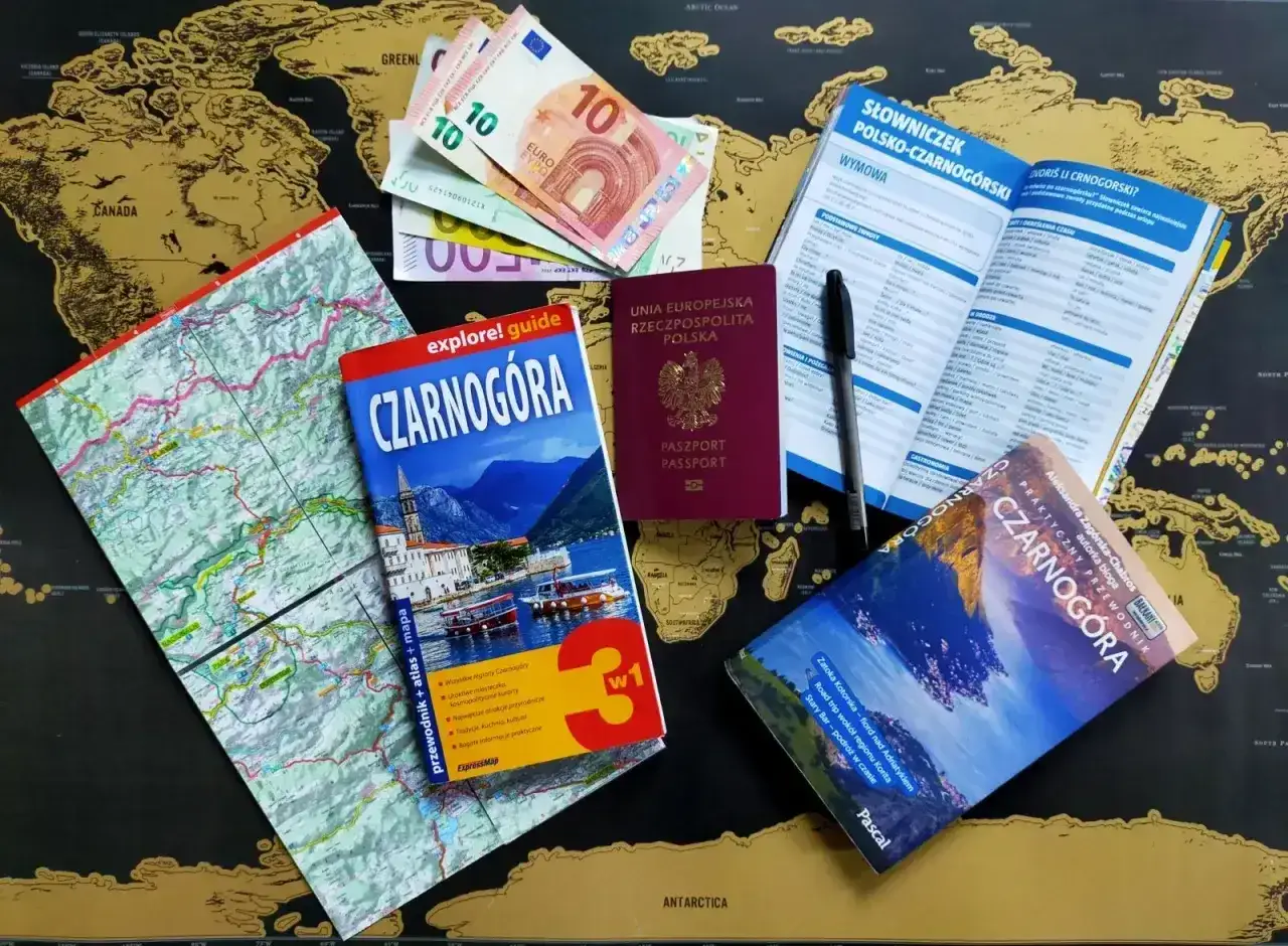 Paszport, pieniądze i przewodniki po Czarnogórze leżą na mapie świata. Czy do Czarnogóry potrzebny jest paszport? Tak, polski paszport jest widoczny.