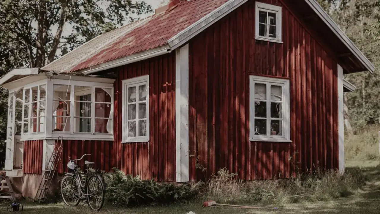 Ett rött trähus med vita fönster och en inglasad veranda. En cykel står parkerad utanför, som om någon nyss kommit hem till detta gamla torp.