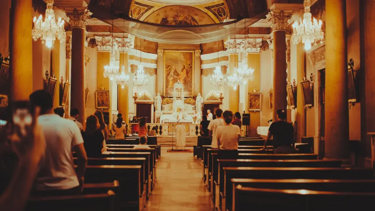 Wnętrze kościoła podczas liturgii mszy świętej. Ludzie siedzą w ławkach, a ksiądz odprawia nabożeństwo przy ołtarzu.