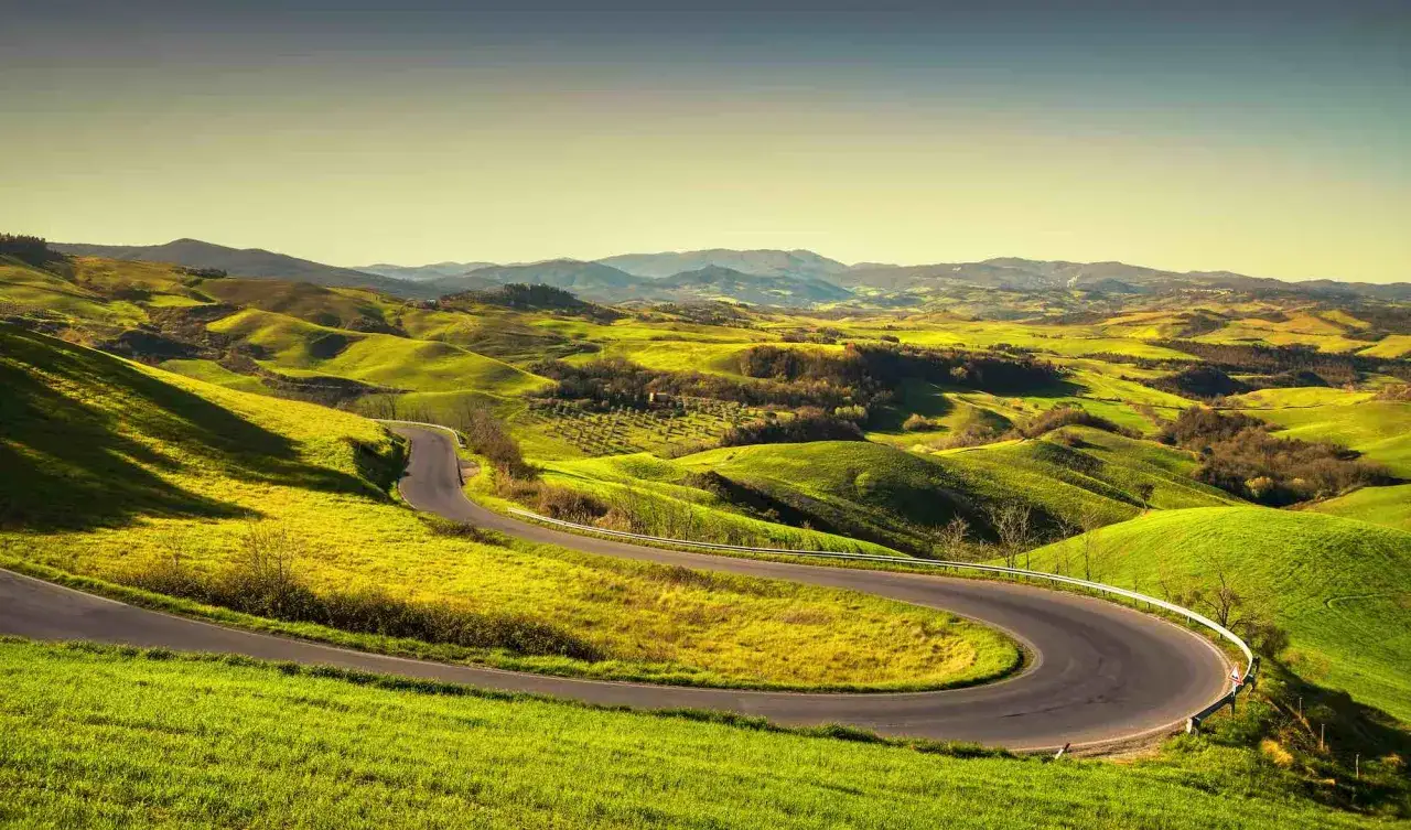 Strade panoramiche toscana serpeggiano tra dolci colline verdi, un invito a esplorare paesaggi mozzafiato sotto un cielo limpido.