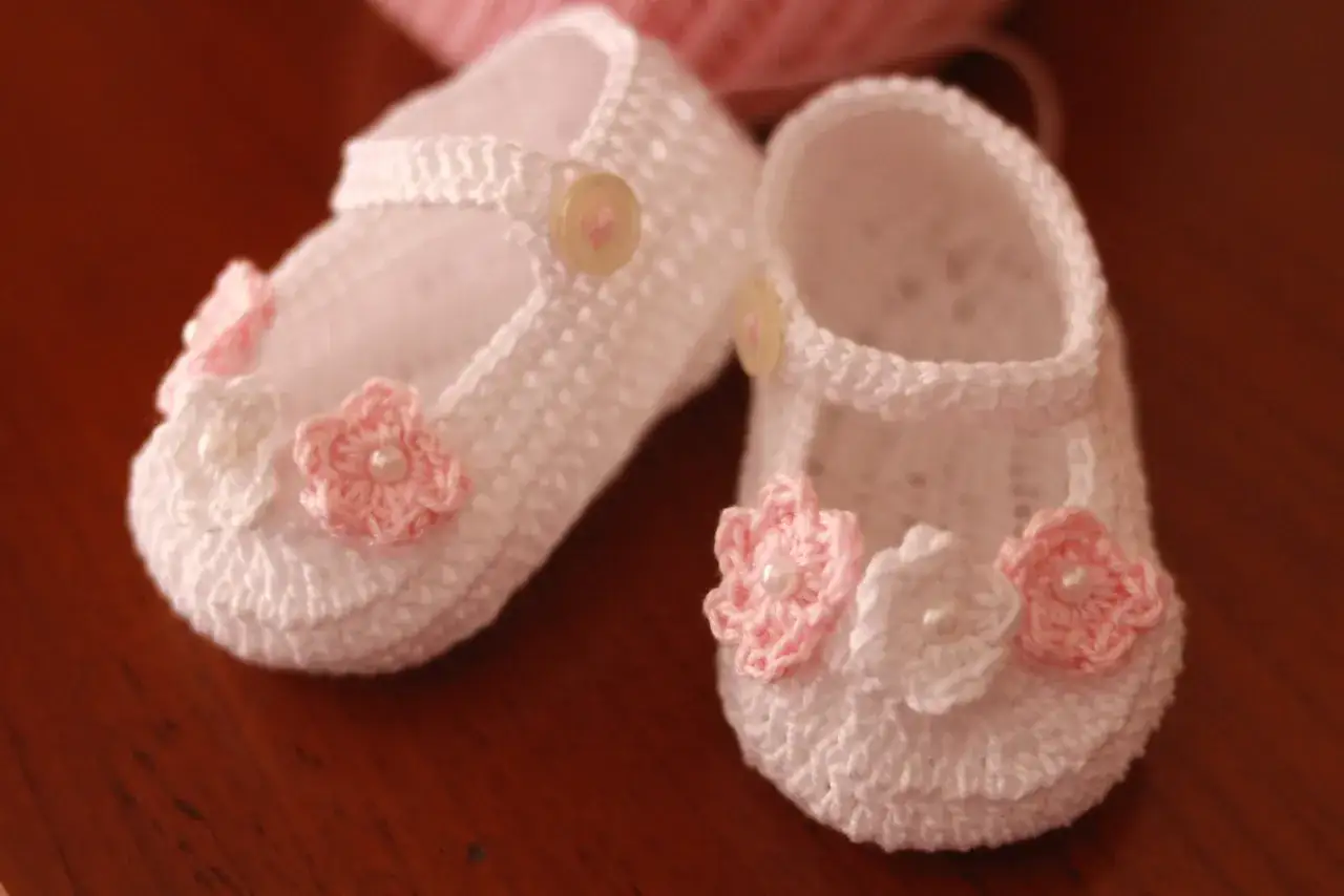 Schemi scarpine neonato uncinetto facilissime: deliziose scarpine bianche con fiori rosa e perle, perfette per un piccolo tesoro.