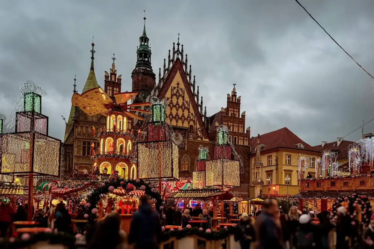 Festlicher wroclaw weihnachtsmarkt mit beleuchteten Geschenkpaketen und einer Weihnachtspyramide vor historischer Architektur.