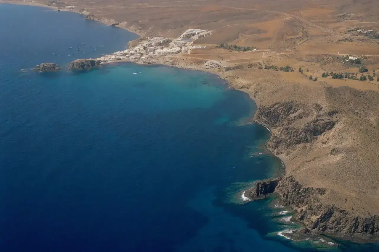 Vista a&eacute;rea de la cala del Pe&ntilde;&oacute;n Blanco, con aguas turquesas, rocas y un peque&ntilde;o pueblo costero.