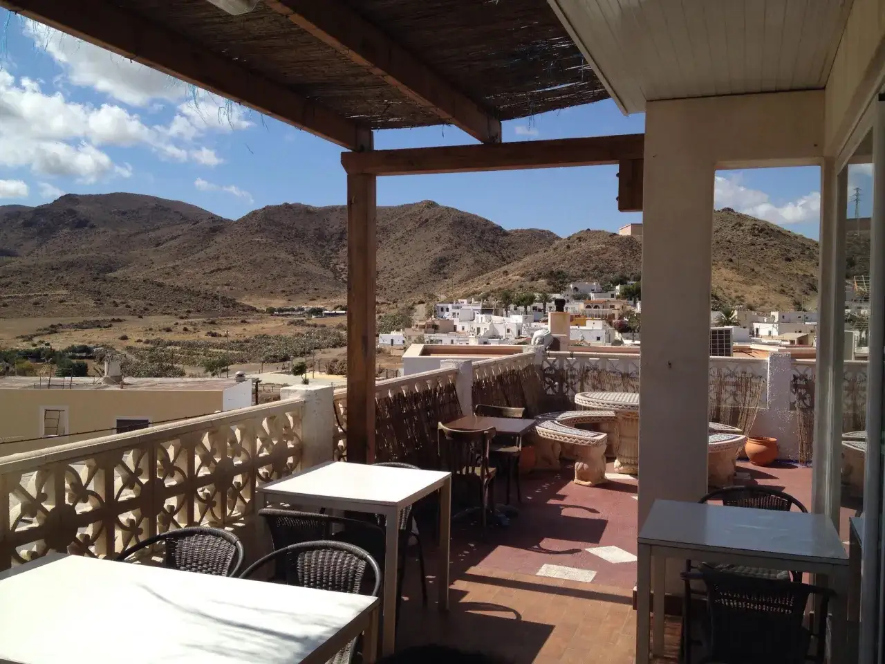 Terraza de el pozo de los frailes restaurantes con vistas a un pueblo y montañas áridas. Mesas y sillas de mimbre y metal.