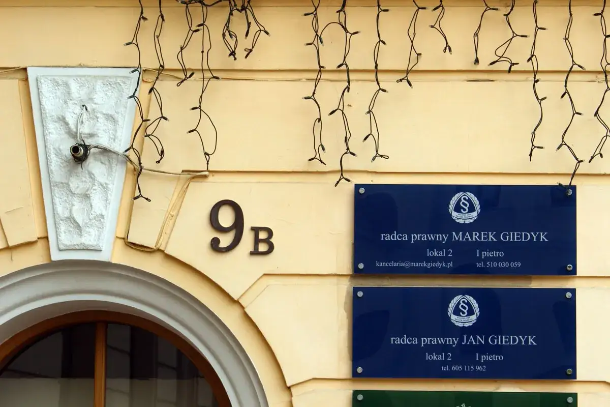 Tablice z nazwami kancelarii prawnych MAREK GIEDYK i JAN GIEDYK na żółtej ścianie budynku.