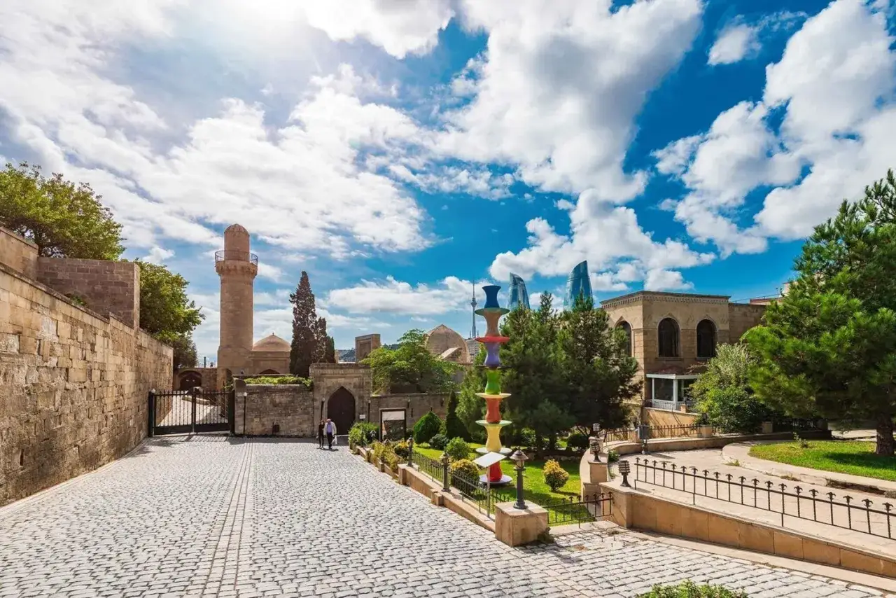 Azerbejdżan co zobaczyć: historyczna wieża meczetu i nowoczesne wieżowce Flame Towers w Baku, z kolorową rzeźbą w centrum.