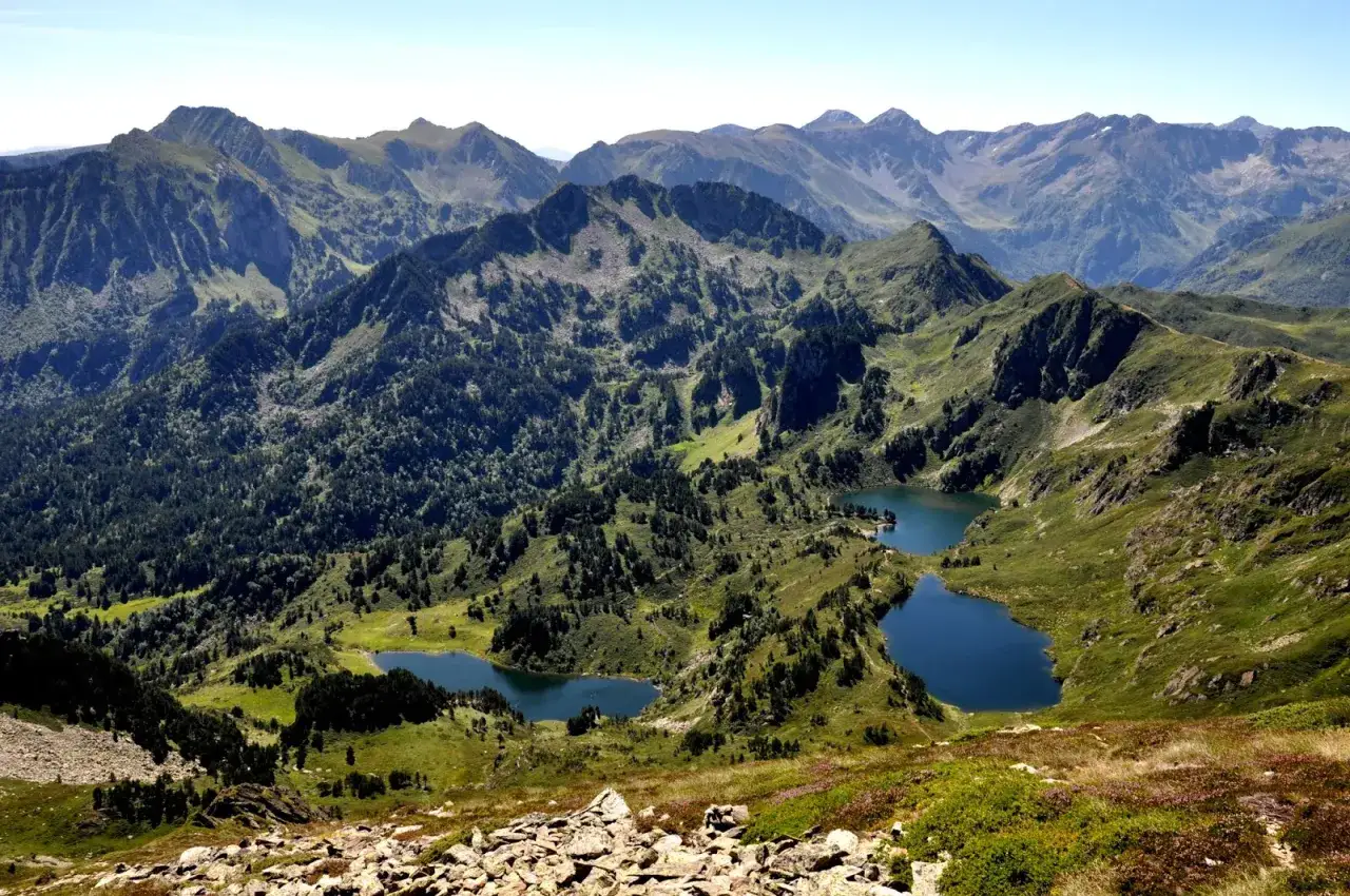 Vue panoramique depuis le pic de Tarbesou, avec des lacs d'altitude bleus nichés au cœur de montagnes verdoyantes et boisées.