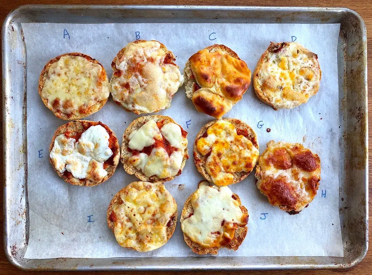Mini pizze z r&oacute;żnymi rodzajami roztopionego sera na blasze. Każda z nich ma sw&oacute;j unikalny wygląd, niekt&oacute;re z lekko przypieczonym serem, inne z bardziej kremowym.