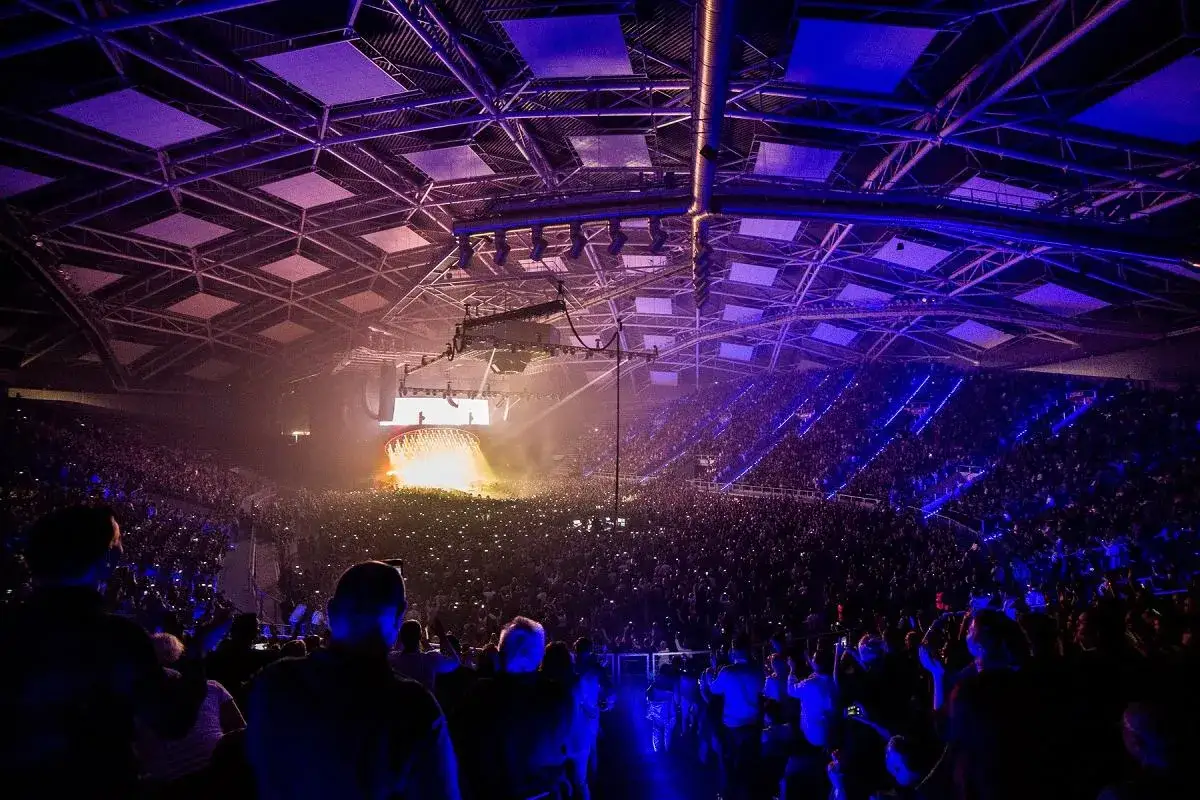 Koncert Queen + Adam Lambert w wypełnionej po brzegi hali. Tłum świeci telefonami, a scena rozświetlona jest jaskrawym światłem.