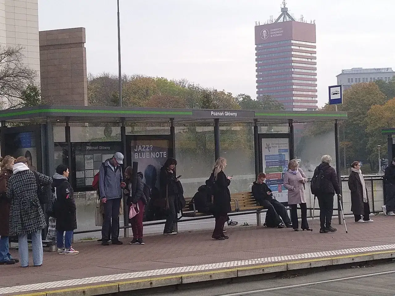 Menschen warten an der Haltestelle Poznań Gł&oacute;wny, ein hoher roter Turm im Hintergrund. Ein **Berlin Posen Zug** k&ouml;nnte hier bald ankommen.