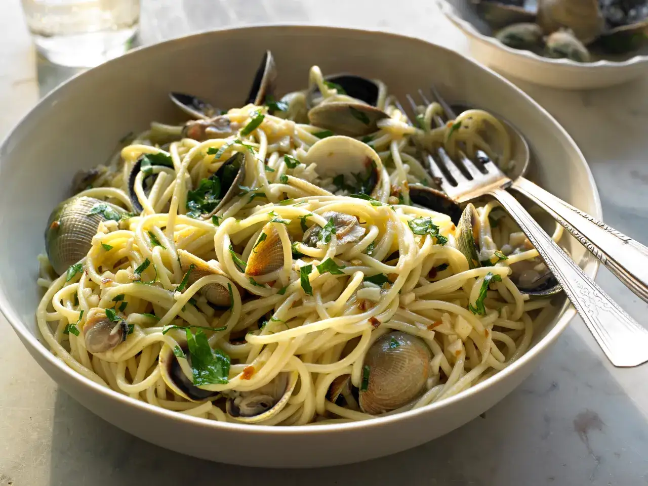 Un plat de spaghetti alle vongole, garni de persil frais et de palourdes, prêt à être dégusté avec une fourchette.
