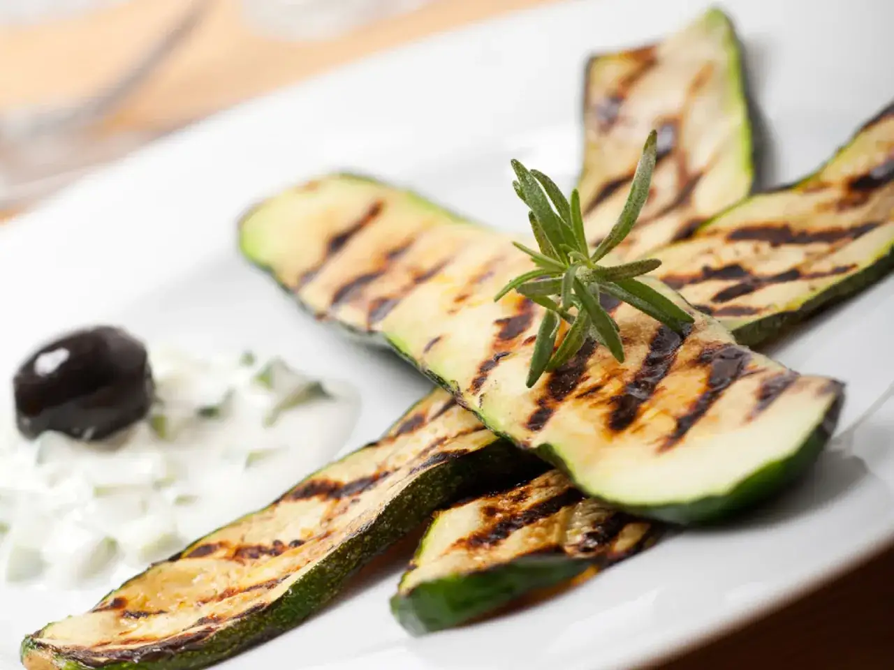 Gegrillte Zucchinischeiben mit Rosmarin, dazu ein Klecks Joghurt-Dip und eine schwarze Olive. Perfekt zum Zucchini grillen!