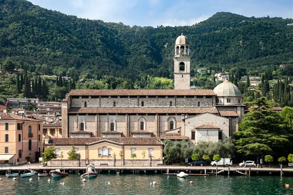 Il **sal&ograve; centro storico** si affaccia sul lago, con un'imponente chiesa e case colorate sullo sfondo di colline verdi.
