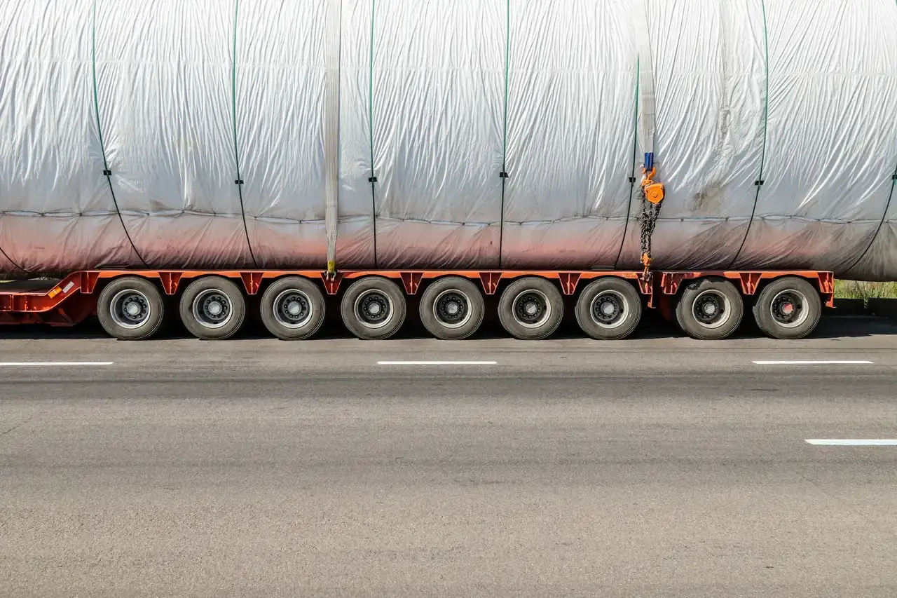 Ogromny ładunek, prawdopodobnie element turbiny, przewożony jest w ramach transportu ponadgabarytowego. Wielokołowa platforma z trudem radzi sobie z jego ciężarem.