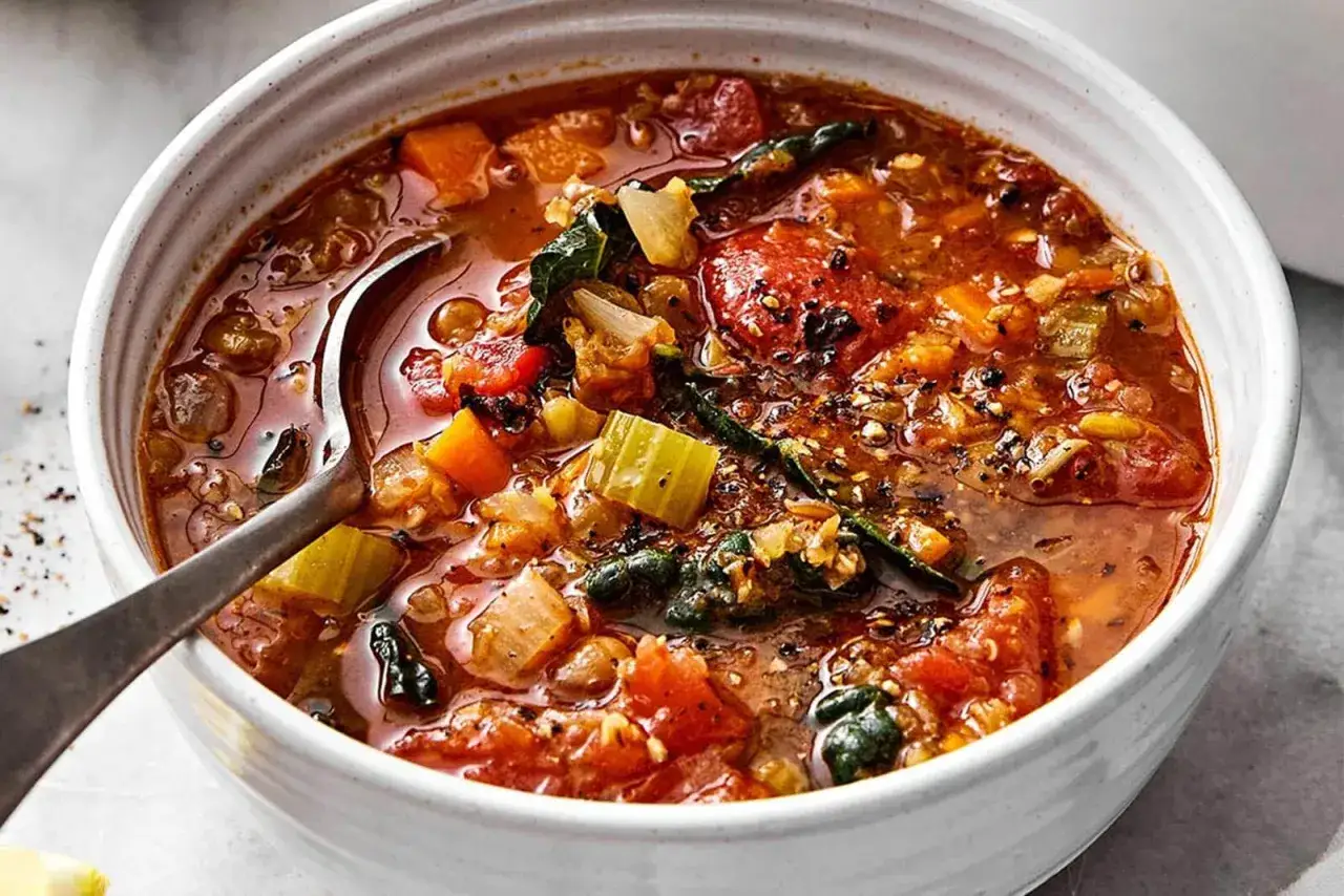 Un bol de soupe réconfortante aux lentilles corail, tomates, carottes et épinards, avec une cuillère en argent.