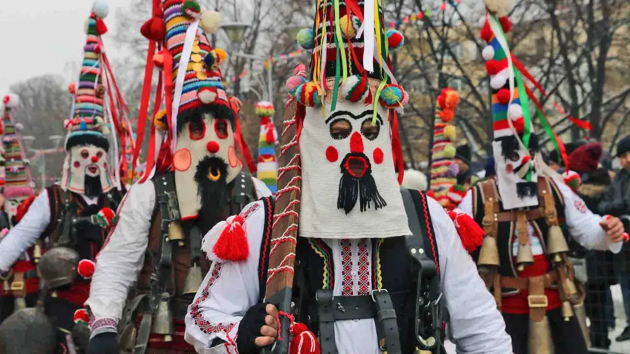 Uomini con maschere spaventose e costumi colorati, parte della tradizione dei kukeri in Bulgaria, sfilano in una parata.