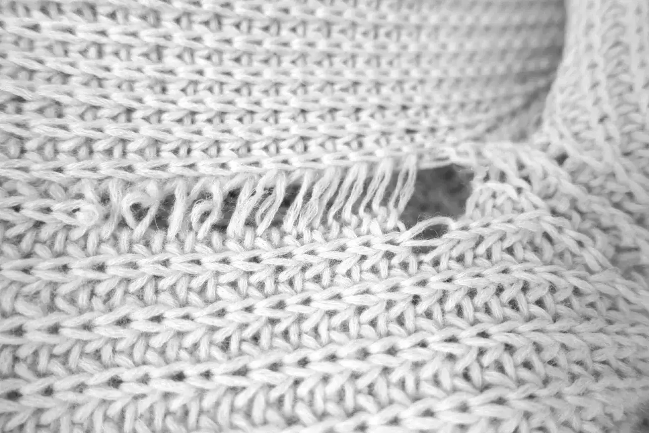 Nahaufnahme eines wei&szlig;en Strickstoffes mit einem Loch und ausgefransten F&auml;den. Was tun, wenn die Wolle eingelaufen ist?