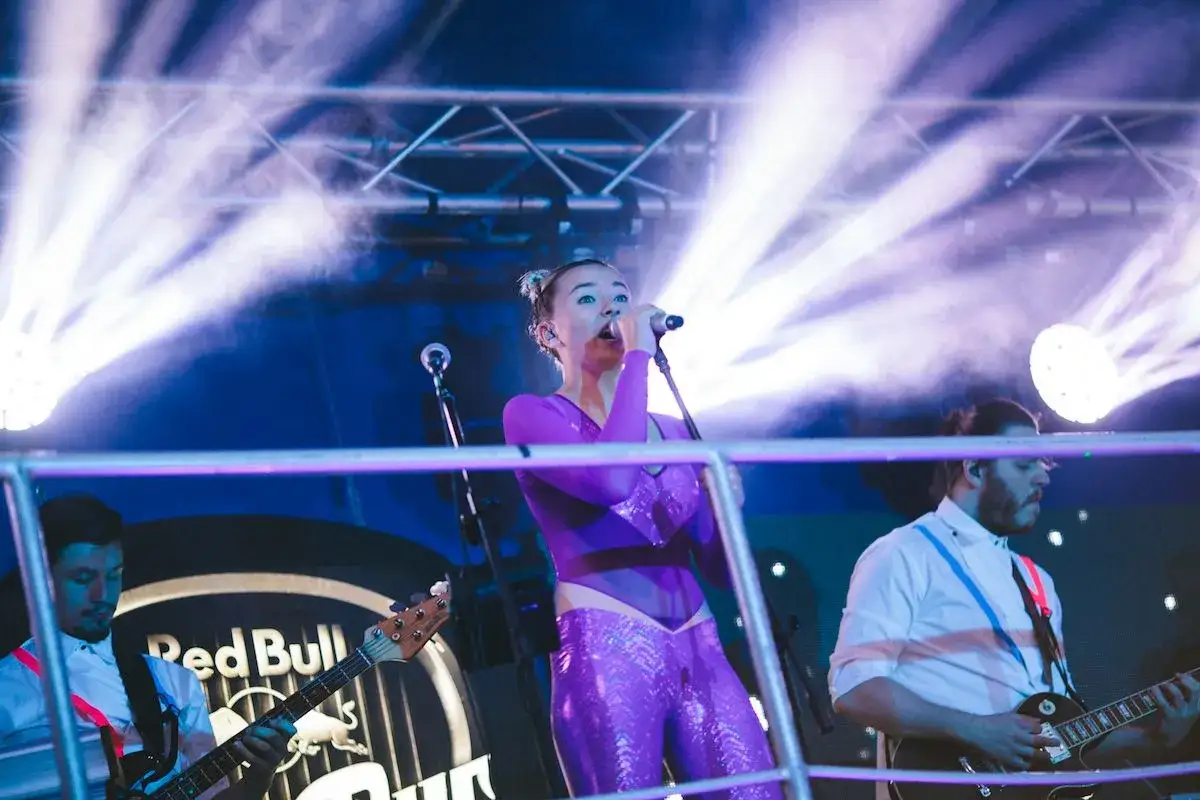 Natalia Nykiel na scenie, w fioletowym stroju, śpiewa swoje utwory. Towarzyszy jej zespół.