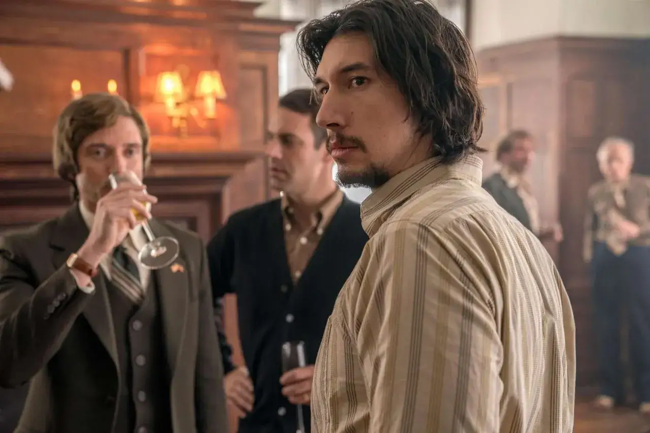 Adam Driver i en randig skjorta, med m&auml;n i bakgrunden. En scen fr&aring;n filmer med Adam Driver.