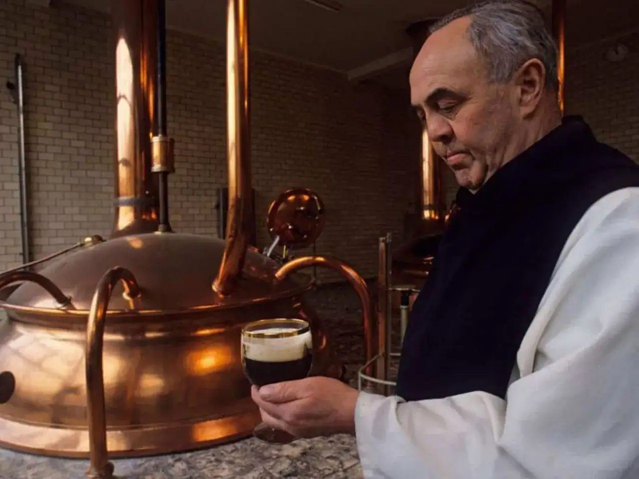 Monaco assaggia una birra scura in una distilleria di abbazie trappiste in Belgio, accanto a grandi alambicchi di rame.