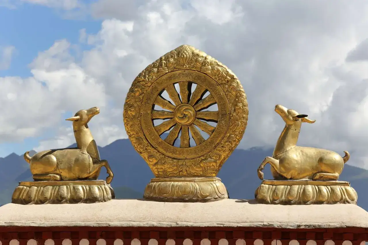 Gyllene Dharma-hjulet, symbol f&ouml;r nirvana inom buddhismen, flankeras av tv&aring; gyllene hjortar mot en molnig himmel.