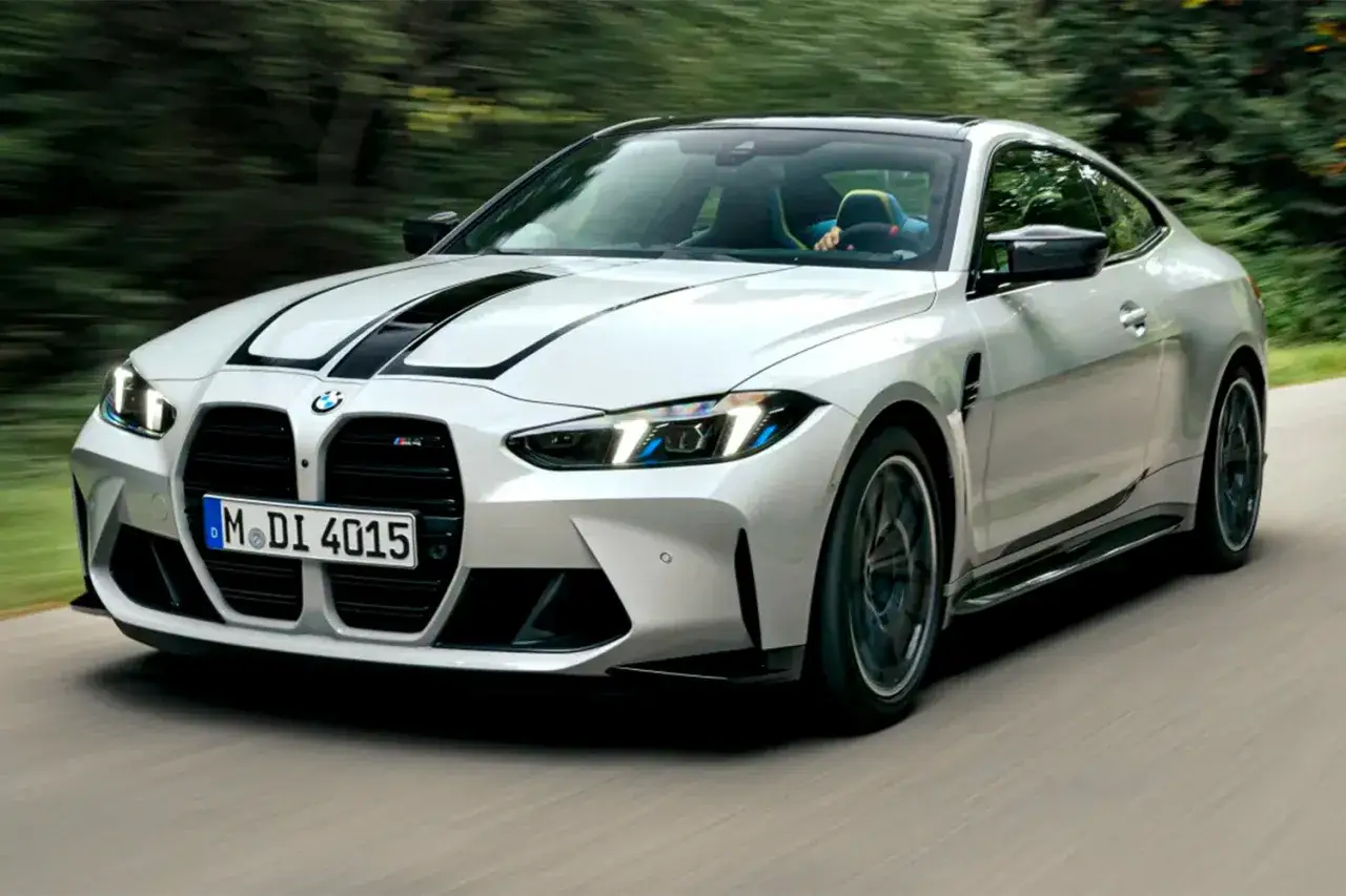 Białe BMW M4 G82 z czarnymi pasami na masce pędzi po drodze wśród zieleni.