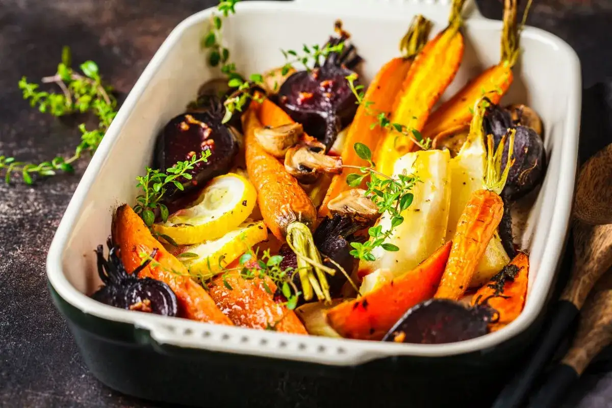 Carote al forno, barbabietole e zucchine arrostite in una teglia, guarnite con timo fresco.